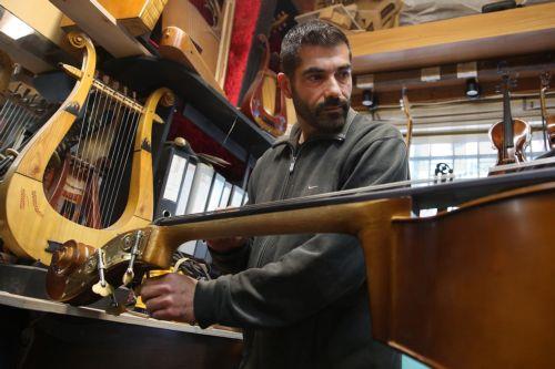 epa12838010 Hercules Bras, with the help of his brother Socrates, tunes a handmade double bass after having installed the bridge on the instrument, in the workshop of their father Nikolas workshop, where handmade stringed instruments have been crafted for 40 years, in Athens, Greece, 26 February 2026 (issued 21 March 2026). The customized shape of these...
