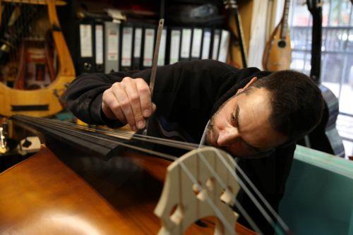 epa12838011 Socrates Bras installs and checks the bridge on a handmade double bass, in his father Nikolas’s workshop, where handmade stringed instruments have been crafted for 40 years, in Athens, Greece, 26 February 2026 (issued 21 March 2026). The customized shape of these hand-crafted instruments, their construction materials, the unique timbre they...