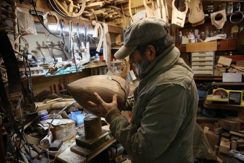 epa12838015 Nikolas Bras examines the bowl (soundbox) of a bouzouki still under construction in his workshop, where he has been working for approximately 40 years crafting handmade stringed instruments, in Athens, Greece, 26 February 2026 (issued 21 March 2026). The customized shape of these hand-crafted instruments, their construction materials, the unique...