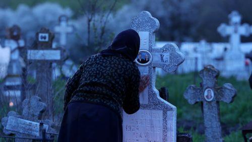 epa12876905 An elderly woman kisses the cross of her family's grave during the Orthodox Maundy Thursday memorial for the departed at a cemetery in Copaciu, Romania, 09 April 2026. Orthodox believers in the village traditionally gather in the early morning to light fires, sprinkle water and smoke over family graves, and share food in memory of their departed...