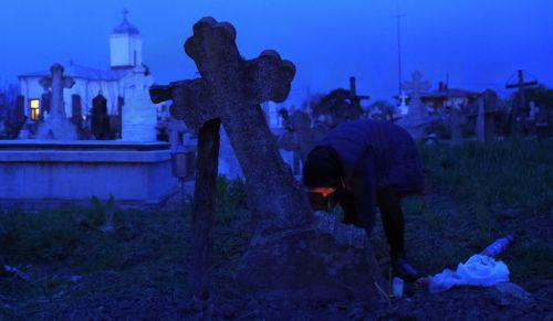 epa12876911 A woman lights a fire of dry branches at her family grave during the Orthodox Maundy Thursday memorial for the departed at a cemetery in Copaciu, Romania, 09 April 2026. Orthodox believers in the village traditionally gather in the early morning to light fires, sprinkle water and smoke over family graves, and share food in memory of their...