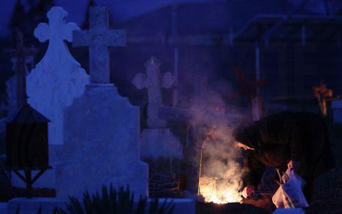 epa12876913 A woman spreads incense smoke over her family grave during the Orthodox Maundy Thursday memorial for the departed at a cemetery in Copaciu, Romania, 09 April 2026. Orthodox believers in the village traditionally gather in the early morning to light fires, sprinkle water and smoke over family graves, and share food in memory of their departed...