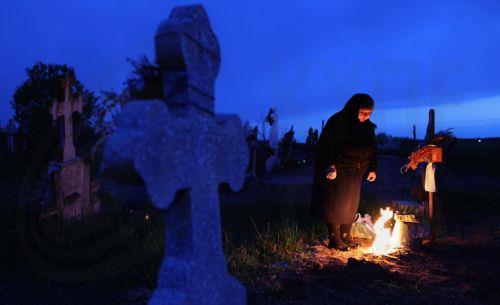 epaselect epa12876909 A woman mourns at her family's grave after lighting a fire of dry branches during the Orthodox Maundy Thursday memorial for the departed at a cemetery in Copaciu, Romania, 09 April 2026. Orthodox believers in the village traditionally gather in the early morning to light fires, sprinkle water and smoke over family graves, and share...