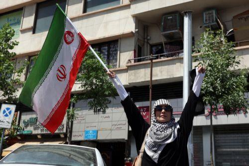 epa12938642 A woman holds Iran's national flag at Enghelab (Revolution) Square in Tehran, Iran, 07 May 2026. US President Donald Trump announced a pause in the operation of escorting ships through the Strait of Hormuz, signaling progress in peace talks with Tehran.  EPA/ABEDIN TAHERKENAREH