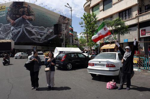 epa12938644 A woman holds Iran's national flag at Enghelab (Revolution) Square in Tehran, Iran, 07 May 2026. US President Donald Trump announced a pause in the operation of escorting ships through the Strait of Hormuz, signaling progress in peace talks with Tehran.  EPA/ABEDIN TAHERKENAREH