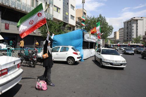 epa12938645 A woman holds Iran's national flag at Enghelab (Revolution) Square in Tehran, Iran, 07 May 2026. US President Donald Trump announced a pause in the operation of escorting ships through the Strait of Hormuz, signaling progress in peace talks with Tehran.  EPA/ABEDIN TAHERKENAREH