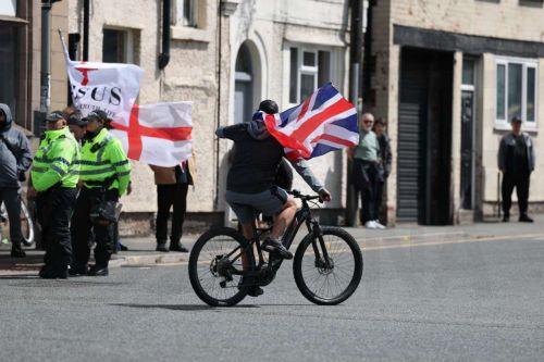 epa13034194 An anti-immigration protester cycles past police on County Road in Liverpool, Britain, 13 June 2026. Anti-immigration protesters calling for 'mass deportation' were met by counter-protesters on County Road, where a community library was burned down during rioting in the wake of the Southport murders in 2024.  EPA/STRINGER