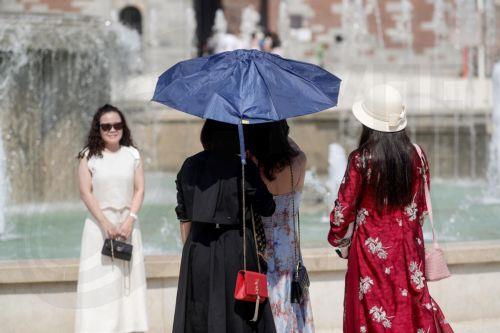 epa13143866 People shelter from the sun under an umbrella on a hot summer day in Milan, Italy, 31 July 2026. The Italian Ministry of Health issued a 'red-dot' heatwave alert for 19 cities starting 01 August. By 02 August, the number of cities under red alert is expected to increase to 23 out of the 27 being monitored.  EPA/MOURAD BALTI TOUATI