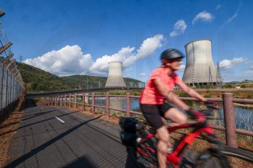 epa13151074 A person cycles past the Chooz nuclear power plant and the River Meuse near Chooz, northeastern France, 05 August 2026. The plant's two reactors have been shut down since 01 August 2026 after prolonged hot and dry weather caused the River Meuse to fall below the level required for cooling operations while maintaining compliance with...