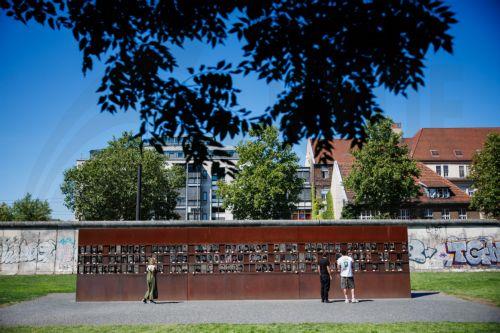 epa13166444 Visitors look at portraits of victims of the Berlin Wall that are part of an installation, decorated with flowers, at the Berlin Wall Memorial after the 65th anniversary commemoration of the construction of the Berlin Wall in Berlin, Germany, 13 August 2026. Some 65 years ago, on 13 August 1961, the Berlin Wall construction started.  EPA/CLEMENS...