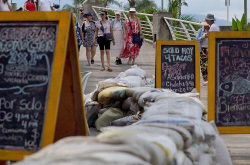 epa13293001 Tourists stroll past businesses and restaurants with barricades in place as Hurricane Simon passes through on Friday; the storm reaches Category 2 in the Mexican Pacific, with sustained winds of 155 kilometers per hour, in Puerto Vallarta, Mexico, 09 October 2026.  EPA/Arturo Montero