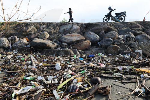 epa13333727 A man walks past a pile of plastic and wooden waste covering a riverbank in Banda Aceh, Indonesia, 27 October 2026. Plastic waste washed down from residential areas via local rivers accumulates along coastal banks before flowing into the sea.  EPA/HOTLI SIMANJUNTAK
