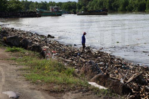 epa13333729 A man walks past a pile of plastic and wooden waste covering a riverbank in Banda Aceh, Indonesia, 27 October 2026. Plastic waste washed down from residential areas via local rivers accumulates along coastal banks before flowing into the sea.  EPA/HOTLI SIMANJUNTAK