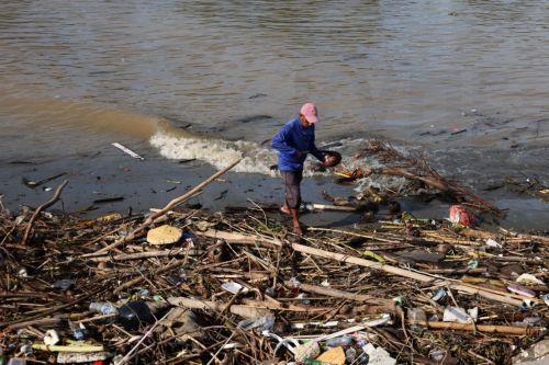 epa13333730 A man walks past a pile of plastic and wooden waste covering a riverbank in Banda Aceh, Indonesia, 27 October 2026. Plastic waste washed down from residential areas via local rivers accumulates along coastal banks before flowing into the sea.  EPA/HOTLI SIMANJUNTAK