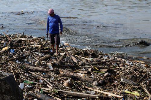 epa13333731 A man walks past a pile of plastic and wooden waste covering a riverbank in Banda Aceh, Indonesia, 27 October 2026. Plastic waste washed down from residential areas via local rivers accumulates along coastal banks before flowing into the sea.  EPA/HOTLI SIMANJUNTAK