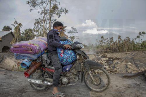 epa10349043 A villager rides his motorbike load with his belongings out of village affected by the eruption of Mount Semeru at Kajar Kuning village in Lumajang, East Java, Indonesia, 05 December 2022. Authorities has raised Mount Semeru alert status to the highest level following its eruption early on 04 December 2022 forcing around two thousands villagers...