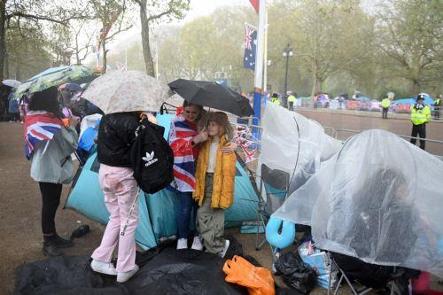 epa10610422 Royal fans shelter from the rain as they wait on the coronation procession route on The Mall in London, Britain, 05 May 2023. Britain's King Charles III's coronation takes place at Westminster Abbey in London on 06 May 2023.  EPA/NEIL HALL