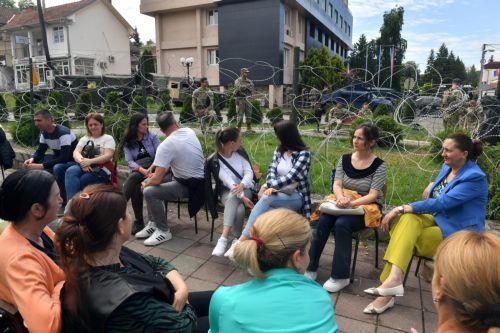 epa10668335 People sit in front of soldiers of the US contingent of the NATO-led international peacekeeping Kosovo Force (KFOR) while they take positions in front of the municipality building in Leposavic, Kosovo, 02 June 2023. At least thirty KFOR peacekeepers and fifty two civilians were injured in clashes between security forces and ethnic Serbs in...