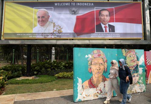 epa11581244 Two Muslim women walk past a banner picturing Pope Francis and Indonesian President Joko Widodo outside the Presidential Palace in Jakarta, Indonesia, 03 September 2024. Pope Francis is on an apostolic visit to the Muslim-majority country from 03 to 06 September and is expected to meet with interfaith leaders at Istiqlal Mosque in Jakarta, the...