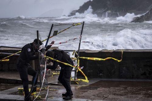 epa11764194 Two police officers struggle with the wind to keep a fence up as a wave breakis at the coast in San Sebastian, Spain, 08 December 2024.  EPA/Javier Etxezarreta