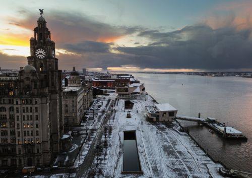 epa11810780 An aerial photograph taken by drone shows  the sun rising behind the Royal Liver building after snow fell overnight in Liverpool, Britain, 07 January 2025. The Met Office has issued further yellow warnings for snow and ice across Northern Ireland and the west coast of Britain after heavy snowfall and rain caused widespread travel disruption and...