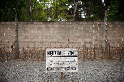 epa12072739 A warning sign in front of a wall equipped with barbed wire reading 'Neutral zone - will be fired upon immediately without announcement' during an event part of the commemorations for the 80th anniversary of the liberation of the former concentration camp Sachsenhausen, in Oranienburg near Berlin, Germany, 04 May 2025. The Sachsenhausen...