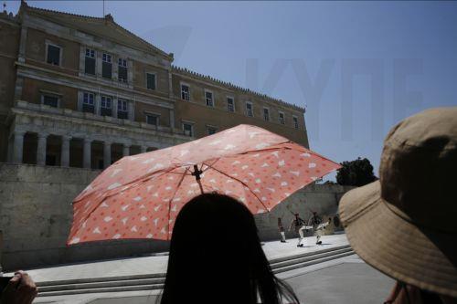 Τουρίστες κρατώντας ομπρέλες και φορώντας καπέλα, για να προστατευτούν από τον ήλιο, παρακολουθούν την αλλαγή της Προεδρικής Φρουράς, στο μνημείο του Αγνώστου Στρατιώτη, κατά τη διάρκεια καύσωνα στην Αθήνα, Πέμπτη 24 Ιουλίου 2025.  Πολύ υψηλή έως και ακραία θερμική επιβάρυνση αναμένεται σήμερα και αύριο σε πολλές περιοχές της Ελλάδας λόγω του ισχυρού...
