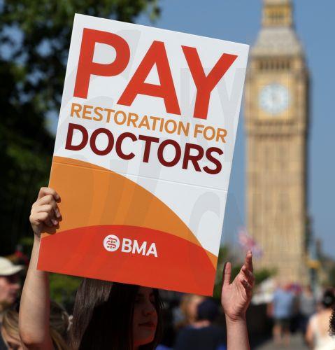 epa12260762 A participant holds a placard as resident doctors rally on strike outside St. Thomas’s hospital in London, Britain, 25 July 2025. Resident doctors have begun a five-day strike across England and Wales over pay and work conditions.  EPA/ANDY RAIN