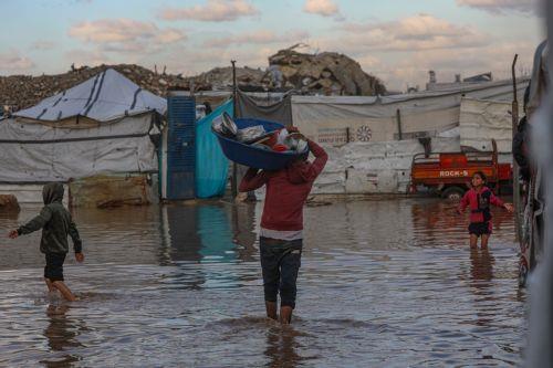epa12548247 Internally displaced Palestinians walk in a puddle near their tents on a rainy day in Al Zaitun neighbourhood in the east of Gaza City, Gaza Strip, 25 November 2025. Around 1.9 million people in Gaza, nearly 90 percent of the population, have been displaced since the Israel-Hamas conflict began in October 2023, according to the UN.  EPA/MOHAMMED...