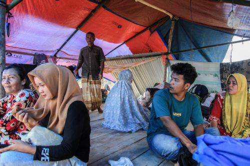 epa12578281 People sit inside a makeshift tent at a flood affected area in Aceh Tamiang, Aceh province, Indonesia, 08 December 2025. According to the National Disaster Management Agency, floods and landslides triggered by Tropical Cyclone Senyar have killed 961 people across the provinces of Aceh, North Sumatra, and West Sumatra, while 293 are reported...