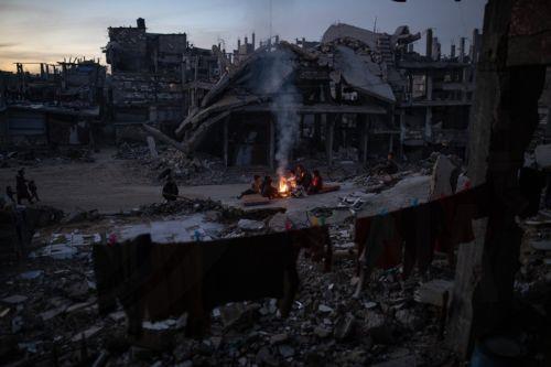 epa12618093 Displaced Palestinians warm themselves near a fire among the ruins of their destroyed home in Khan Yunis, southern Gaza Strip, 30 December 2025, amid a ceasefire between Israel and Hamas.  EPA/HAITHAM IMAD