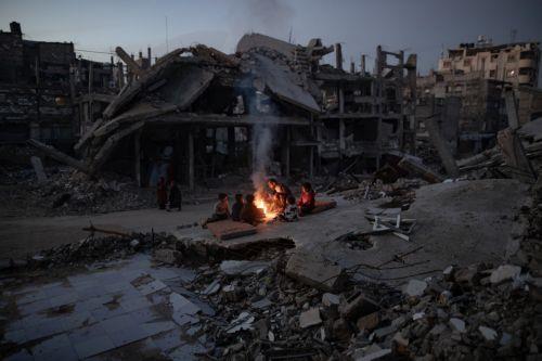 epa12618096 Displaced Palestinians warm themselves near a fire among the ruins of their destroyed home in Khan Yunis, southern Gaza Strip, 30 December 2025, amid a ceasefire between Israel and Hamas.  EPA/HAITHAM IMAD