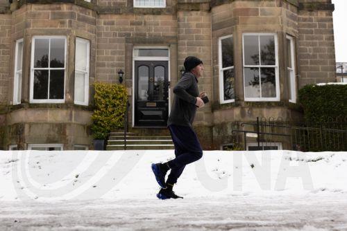 epa12637957 A person jogs along a snow-covered street in Buxton, Britain, 09 January 2026. Met Office yellow and amber warnings for ice, snow and wind remain in force across much of Britain after Storm Goretti, the first named storm of the year, brought heavy snowfall and strong winds.  EPA/ADAM VAUGHAN