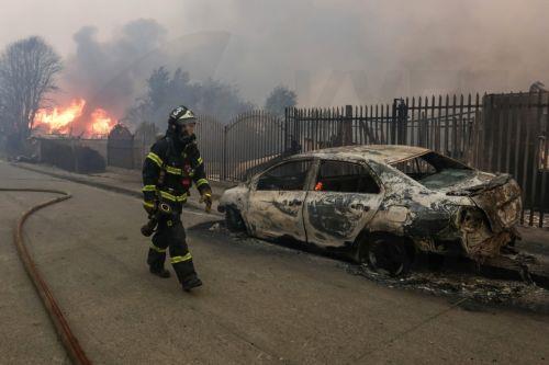 epa12660283 A member of the Chilean Fire Department walks past a vehicle damaged by wildfires in Penco, Chile, 18 January 2026. Chilean President Gabriel Boric announced on 18 January 2026 that the death toll from the wildfires in the southern regions of Nuble and Biobio had risen to 18.  EPA/PABLO HIDALGO